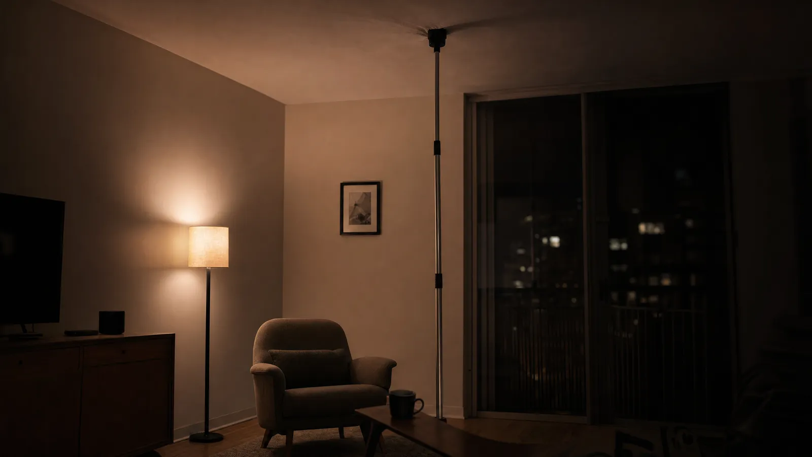 A telescoping ceiling thumper pole propped against an apartment ceiling in a dim living room at night