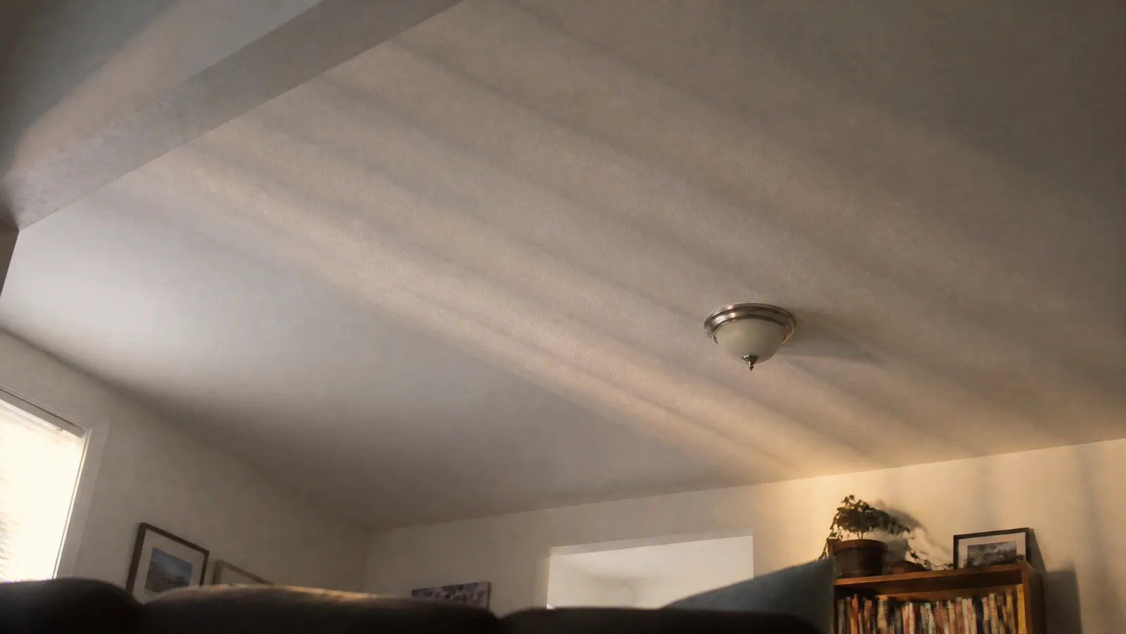 Looking up at an apartment living room ceiling with faint joist shadows in late afternoon light